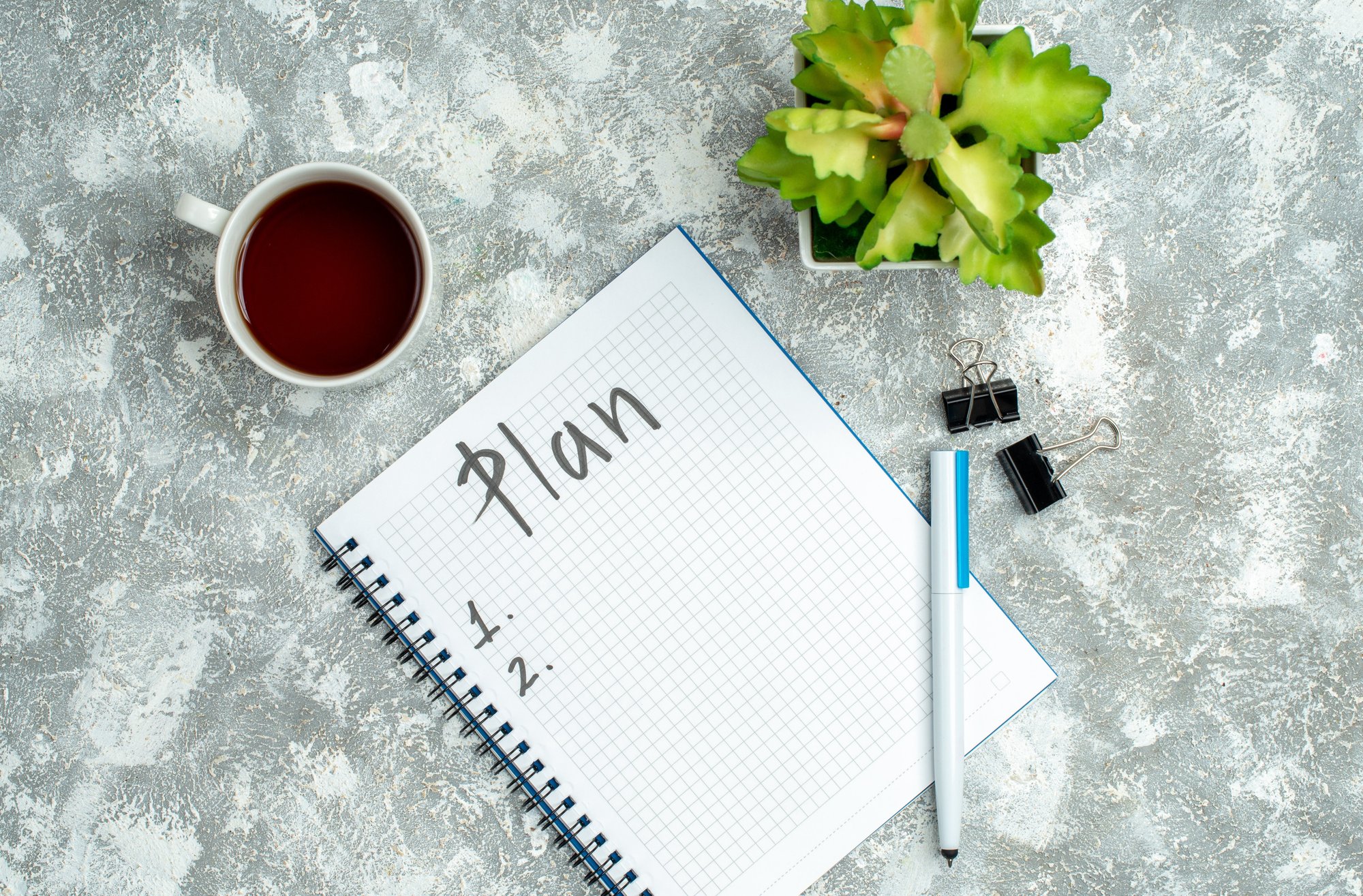 overhead-view-written-spiral-notebook-flower-pot-cup-tea-gray-background